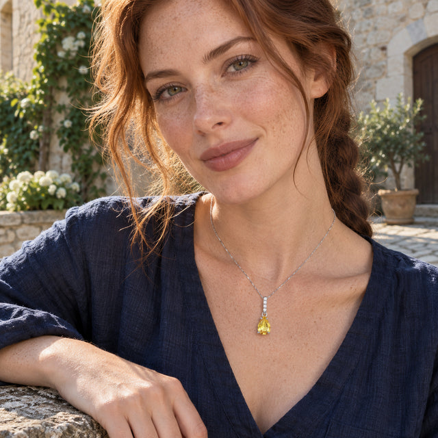 A freckled woman in a navy shirt wears a silver-toned citrine necklace in a stone courtyard with climbing greenery.