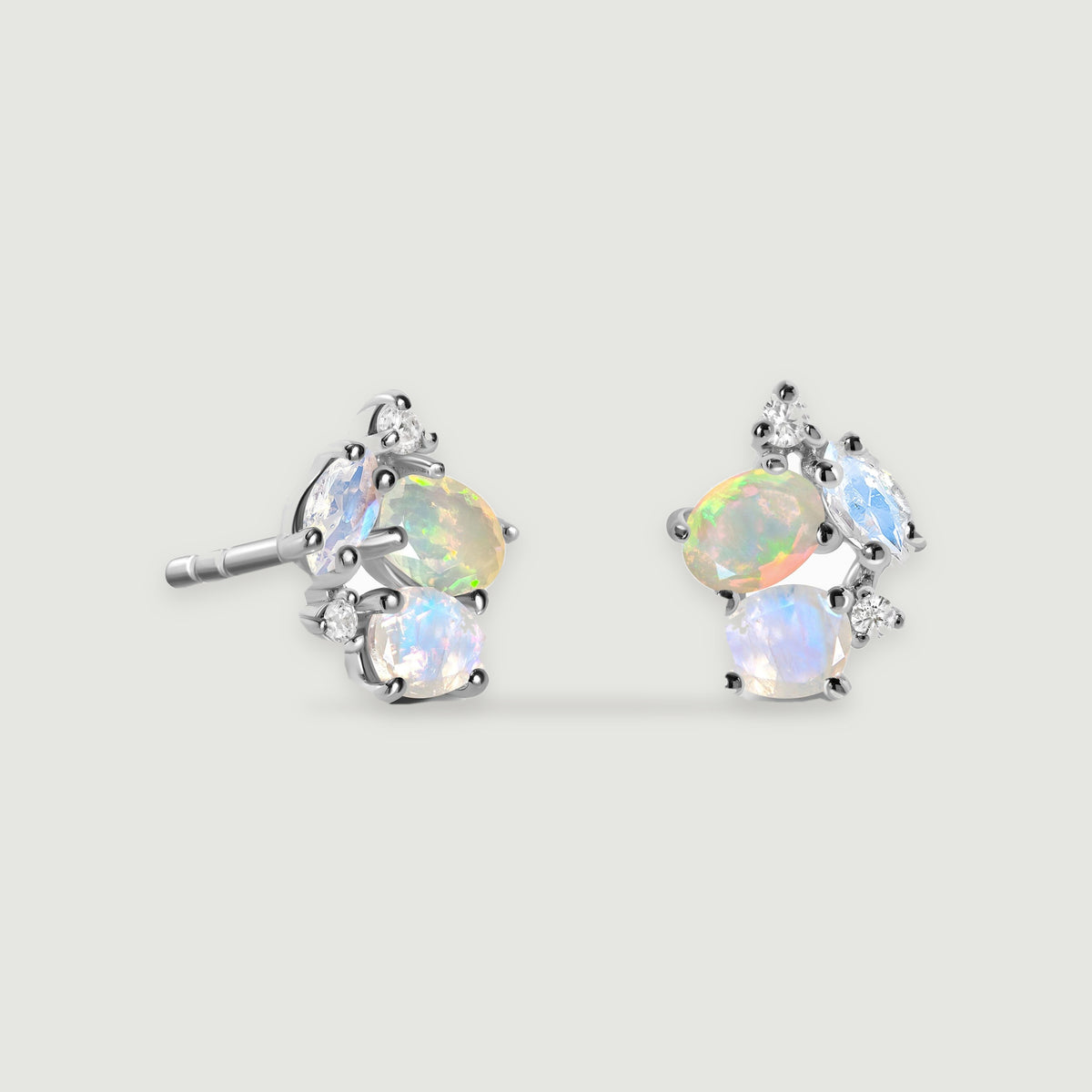 Two silver stud earrings show pale blue stones, colorful opals and small clear accents against light gray.