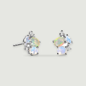 Two silver stud earrings show pale blue stones, colorful opals and small clear accents against light gray.