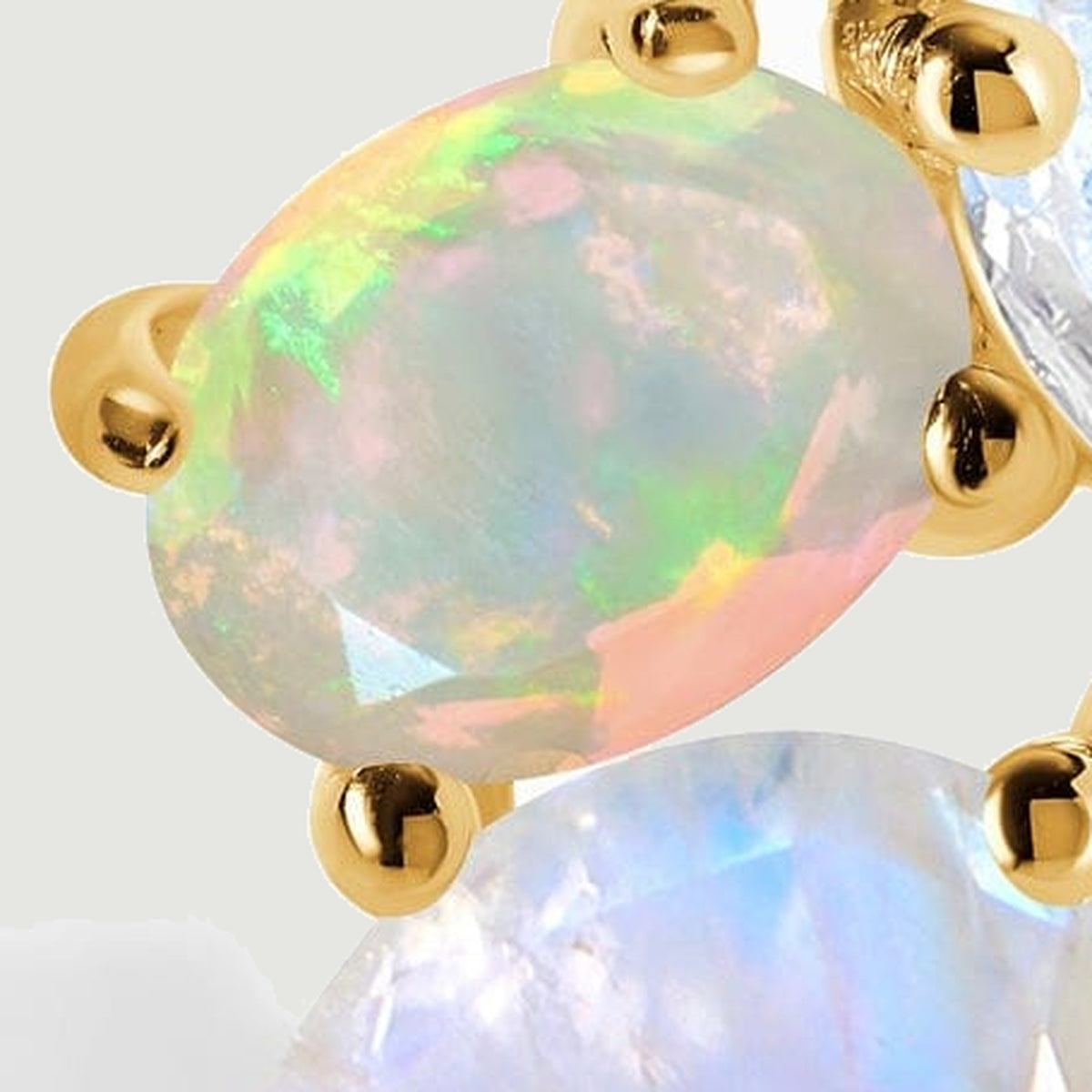 An oval opal reflects green and pink light between polished yellow gold prongs in a tightly cropped detail.