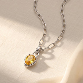 A white rhodium plated citrine pendant lies on cream fabric with its linked chain curving above it.