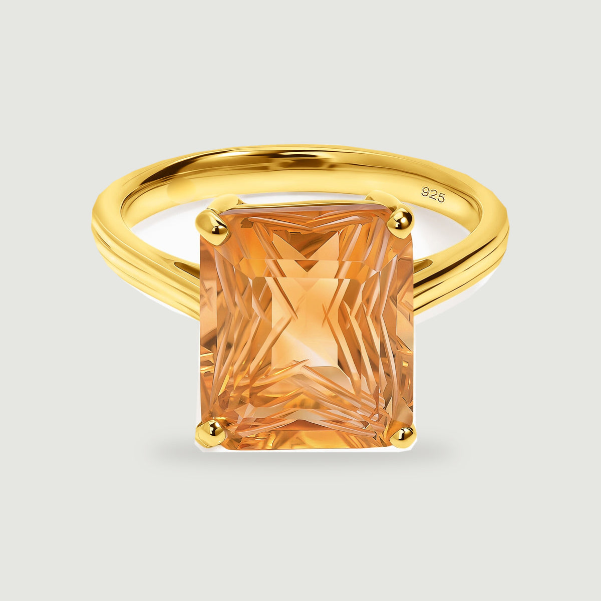 A yellow gold ring with a rectangular citrine and four rounded prongs rests against a soft gray background.
