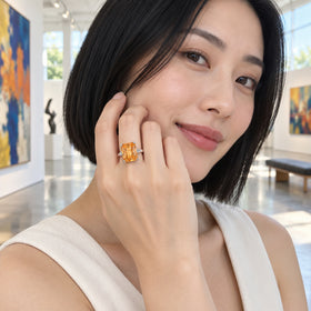 A woman with a black bob wears a silver citrine ring beside her cheek in a bright art gallery.