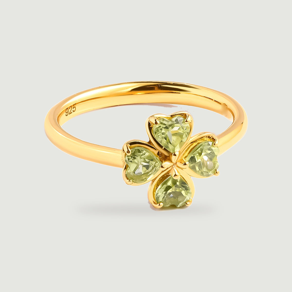A yellow gold vermeil ring displays four heart-shaped green peridot stones on a light gray surface.