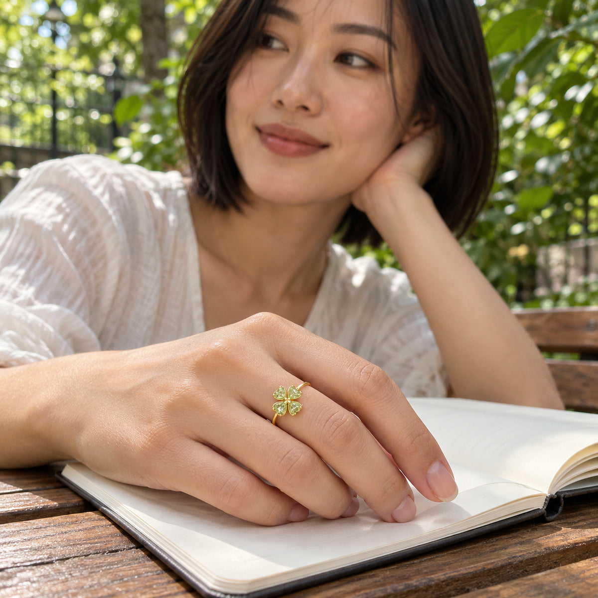 A woman with a dark bob wears the gold peridot ring while resting her hand on an open notebook beside garden greenery.