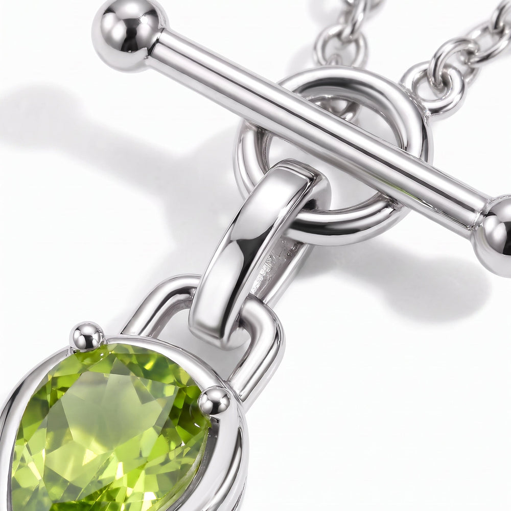 A close view shows the reflective silver-tone bar, circular link and green stone facets.