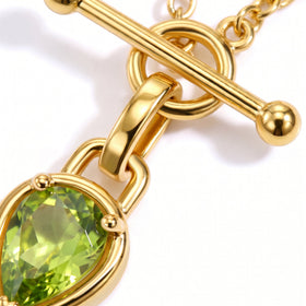 Polished gold-tone links and rounded bar ends sit above the edge of a faceted green pendant.
