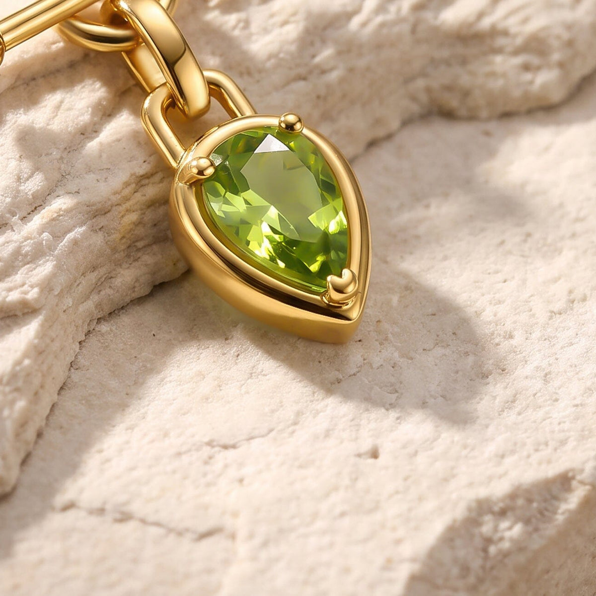 An angled close-up shows the green gemstone held by three rounded prongs inside a gold-tone pear-shaped setting.