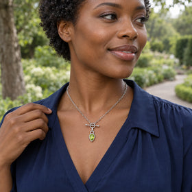 A woman in a navy blouse wears the silver-tone green pear pendant necklace beside a leafy garden path.