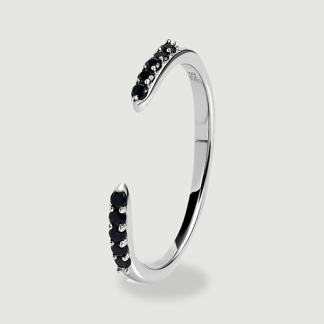 The silver ring is shown upright with a slim polished band and black stones along its open ends.
