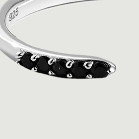 Round black stones sit in bright silver prongs at the near end of the open ring.
