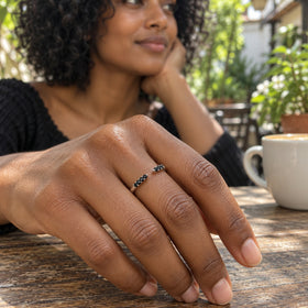 A woman wears the silver open black stone ring on her middle finger at an outdoor cafe table beside a white cup.