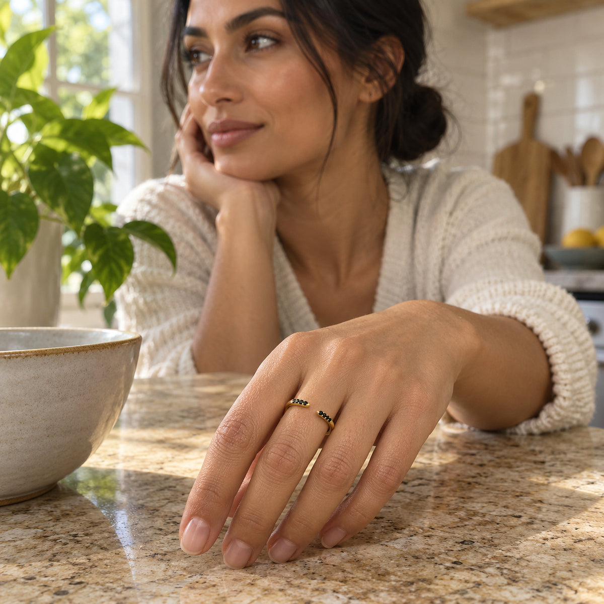 A woman wears the yellow gold vermeil black stone ring while resting her hand on a kitchen stone counter beside a ceramic bowl.