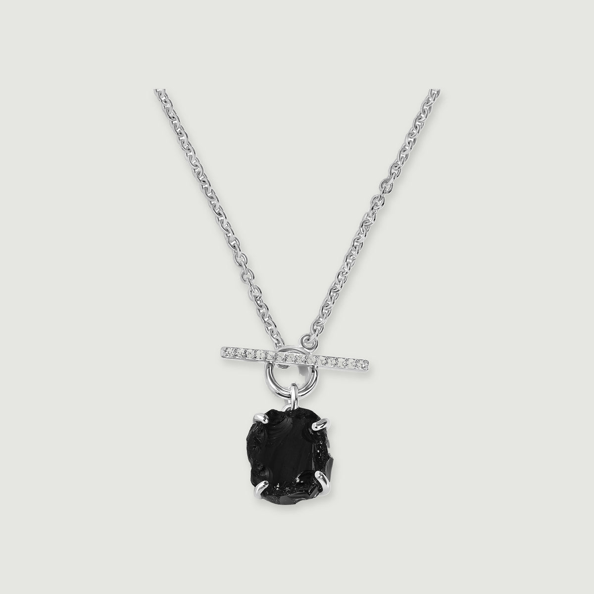 A black obsidian pendant hangs below a crystal-set silver bar and round clasp on a silver chain against a light gray background.