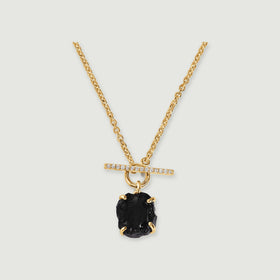 A yellow gold vermeil chain holds a rough black obsidian stone beneath a sparkling horizontal bar on a soft gray surface.