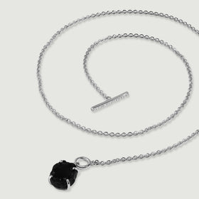 A silver necklace lies in loose curves with its crystal-set bar separated from the circular clasp beside a black obsidian pendant.