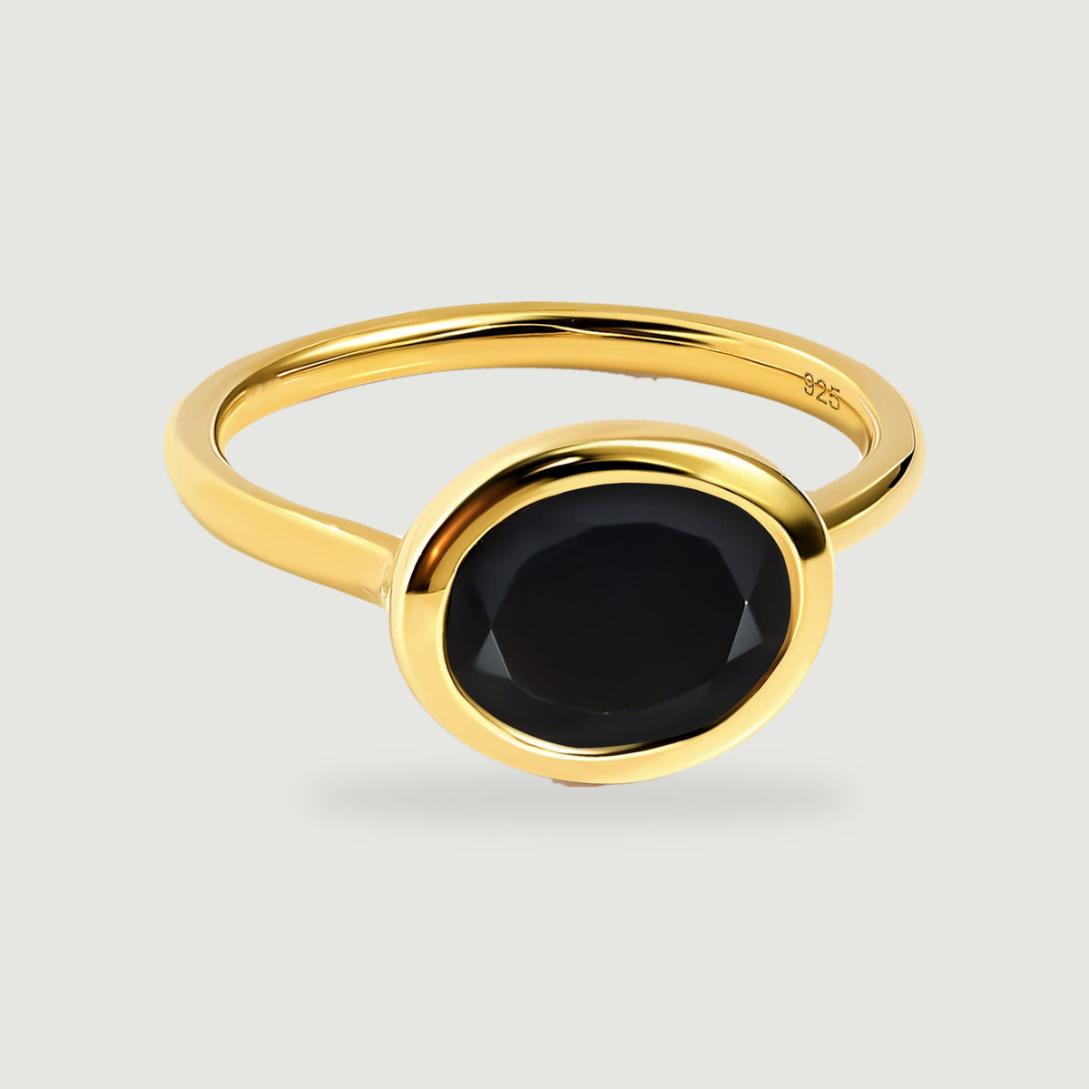 A yellow gold vermeil ring with a faceted oval black stone rests on a light gray background.