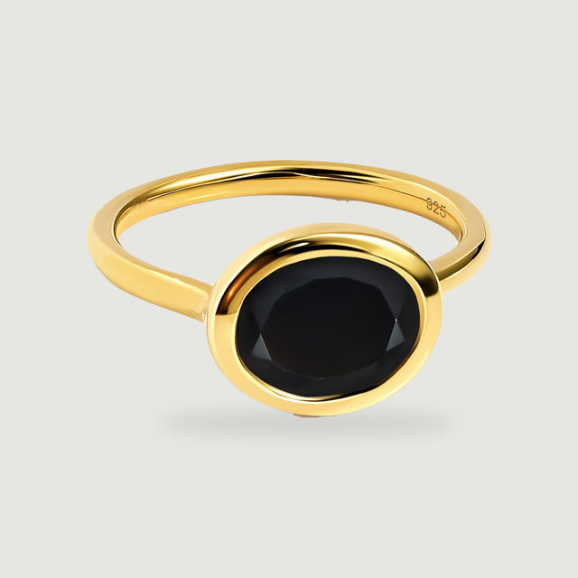 A yellow gold vermeil ring with a faceted oval black stone rests on a light gray background.