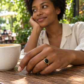 A woman with short curls wears the yellow gold vermeil black stone ring beside a ceramic cup at an outdoor cafe.