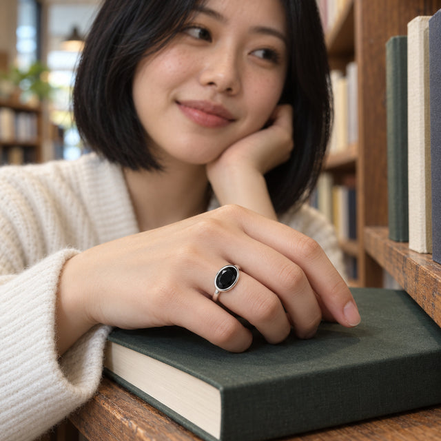 A woman with a dark bob wears the sterling silver black stone ring with her hand resting on a green book.