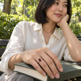 The red garnet ring in rose gold is shown on a hand resting on a closed book outdoors.