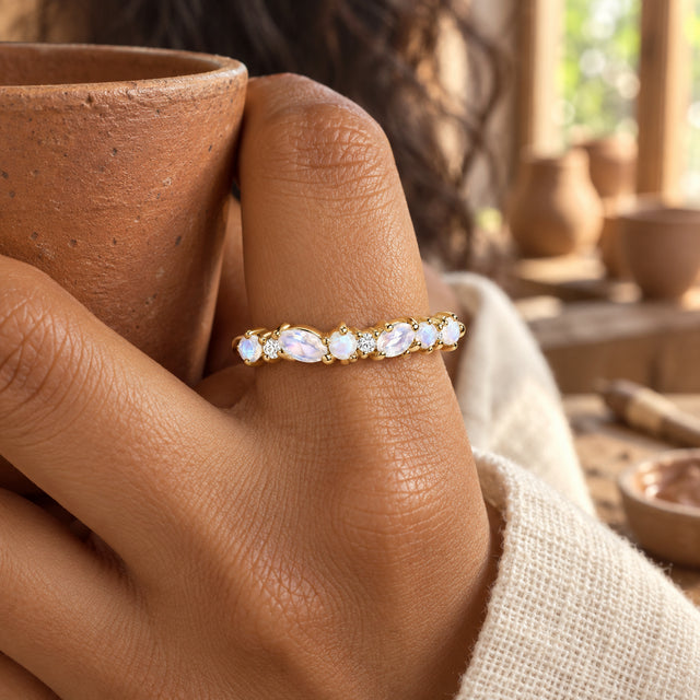 A yellow gold gemstone ring is worn on a warm brown hand holding a terracotta cup.