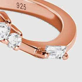 A rectangular clear stone sits beside round stones on the polished rose gold shoulder.