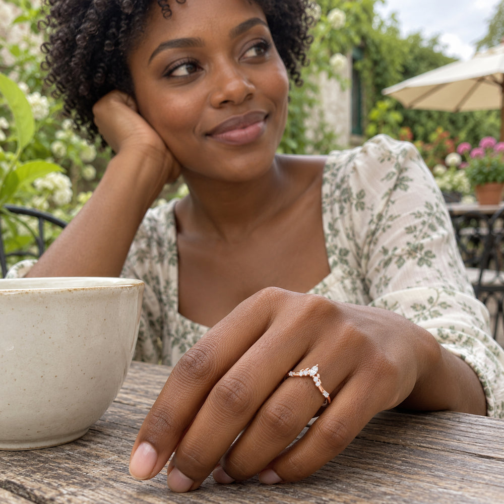 A rose gold ring with clear stones is worn on a hand resting beside a ceramic cup at a garden cafe.