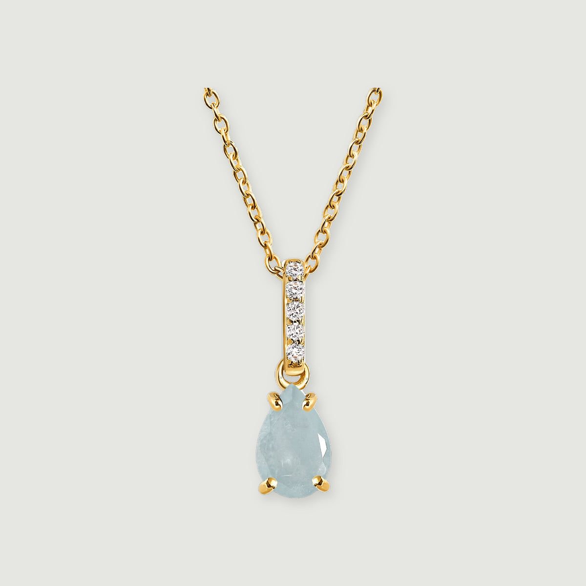 A pale blue pear-shaped pendant hangs below a diamond-set bail on a yellow gold necklace against light gray.