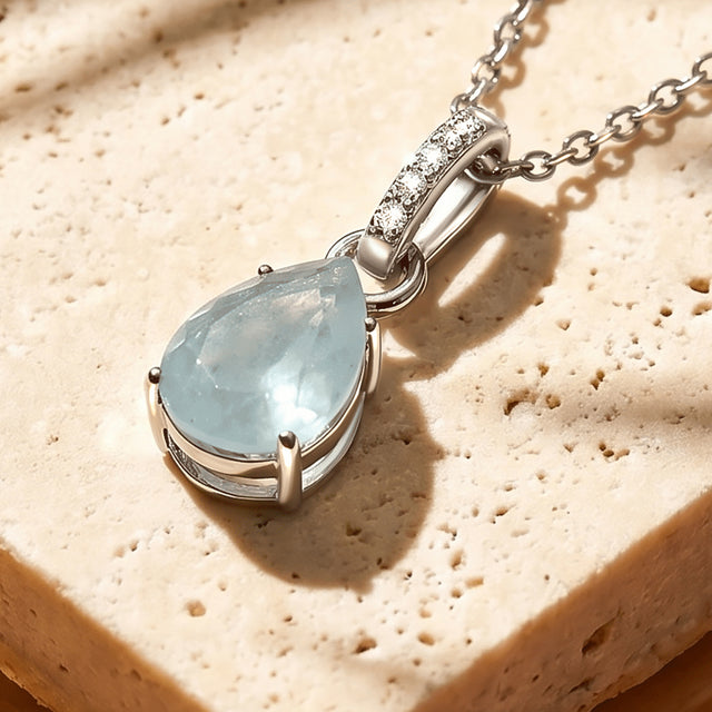 An angled view shows the raised silver prongs, open basket and diamond-set bail around the blue pendant.