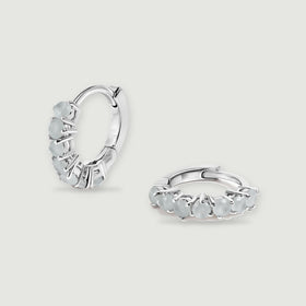 A pair of silver-toned aquamarine hoop earrings rests on a light gray background.