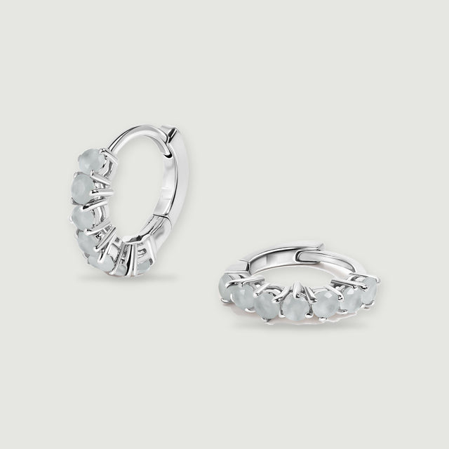 A pair of silver-toned aquamarine hoop earrings rests on a light gray background.