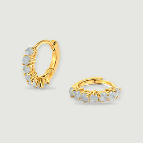 A pair of yellow gold-toned aquamarine hoop earrings rests on a light gray background.
