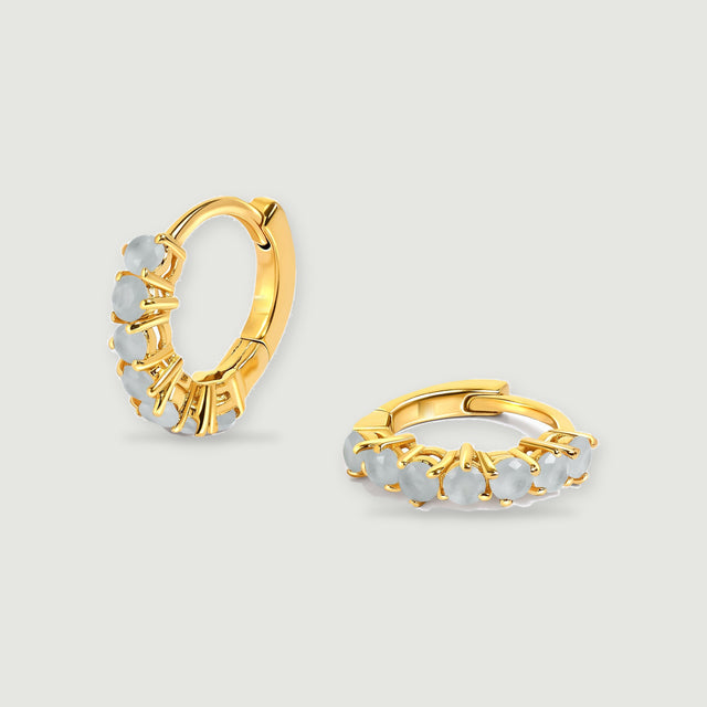A pair of yellow gold-toned aquamarine hoop earrings rests on a light gray background.