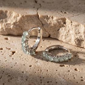 Two silver-toned aquamarine hoops sit on a textured beige stone surface.