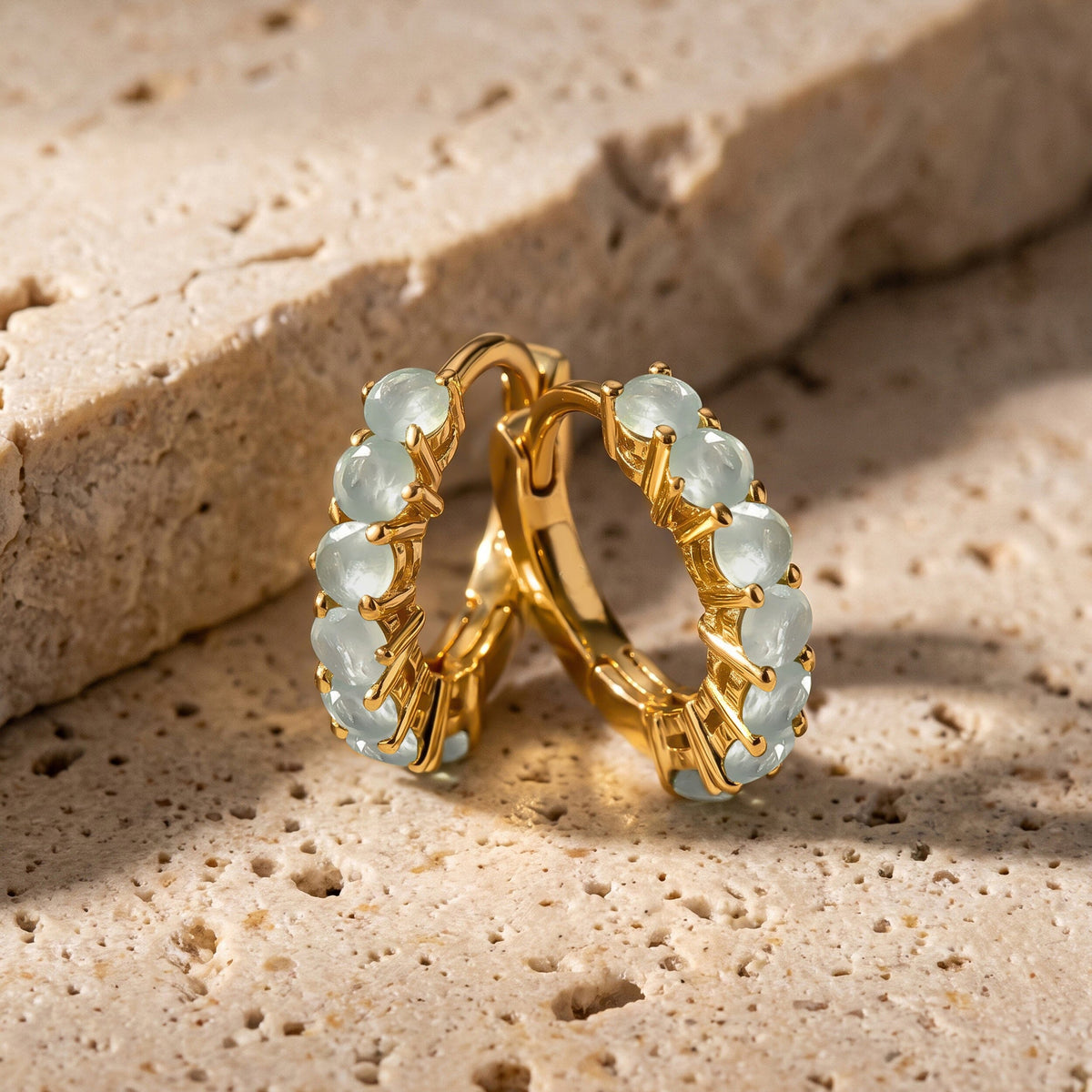 A pair of yellow gold-toned aquamarine hoops stands together on a beige stone tabletop.