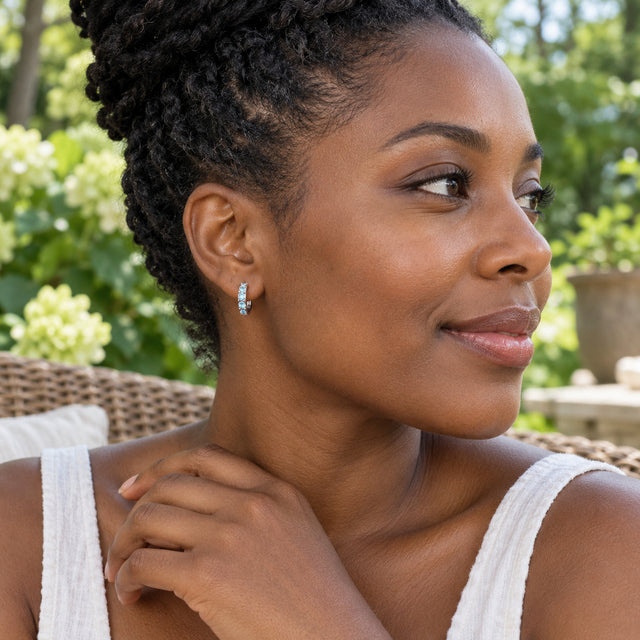A woman with braided dark hair wears a silver-toned aquamarine hoop on a leafy garden patio.