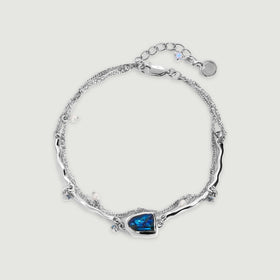 A sterling silver bracelet forms an oval around an open center, with a blue labradorite setting and small pearl charms on a pale gray background.