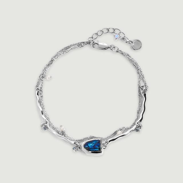 A sterling silver bracelet forms an oval around an open center, with a blue labradorite setting and small pearl charms on a pale gray background.