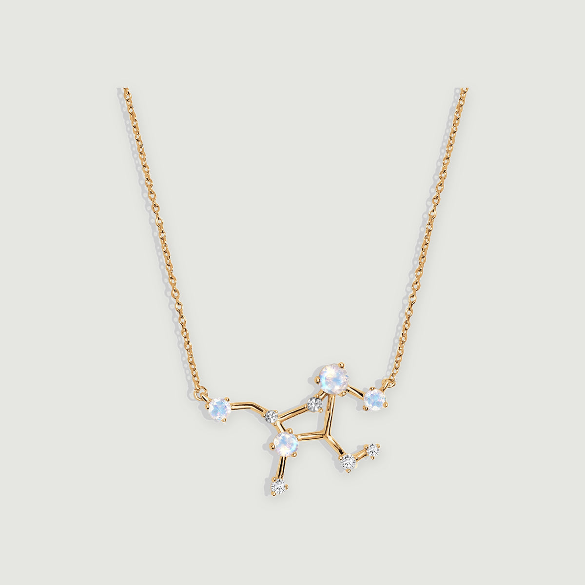 A yellow gold necklace displays round moonstones and small clear stones along an angular pendant on light grey.