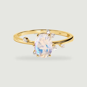 A yellow gold ring displays an oval faceted moonstone and scattered round diamond accents on a light gray background.