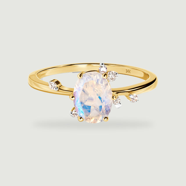 A yellow gold ring displays an oval faceted moonstone and scattered round diamond accents on a light gray background.