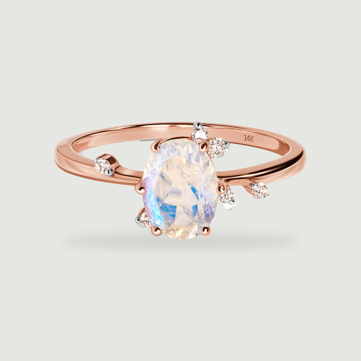 A rose gold ring rests at a front angle with an oval moonstone and small round diamonds beside its polished band.