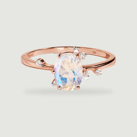 A rose gold ring rests at a front angle with an oval moonstone and small round diamonds beside its polished band.