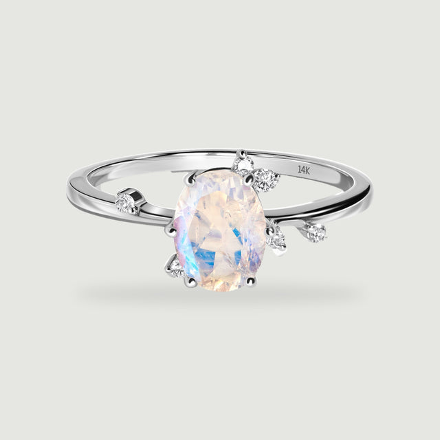 A white gold ring shows a pale oval moonstone with blue reflections and round diamond accents around the setting.