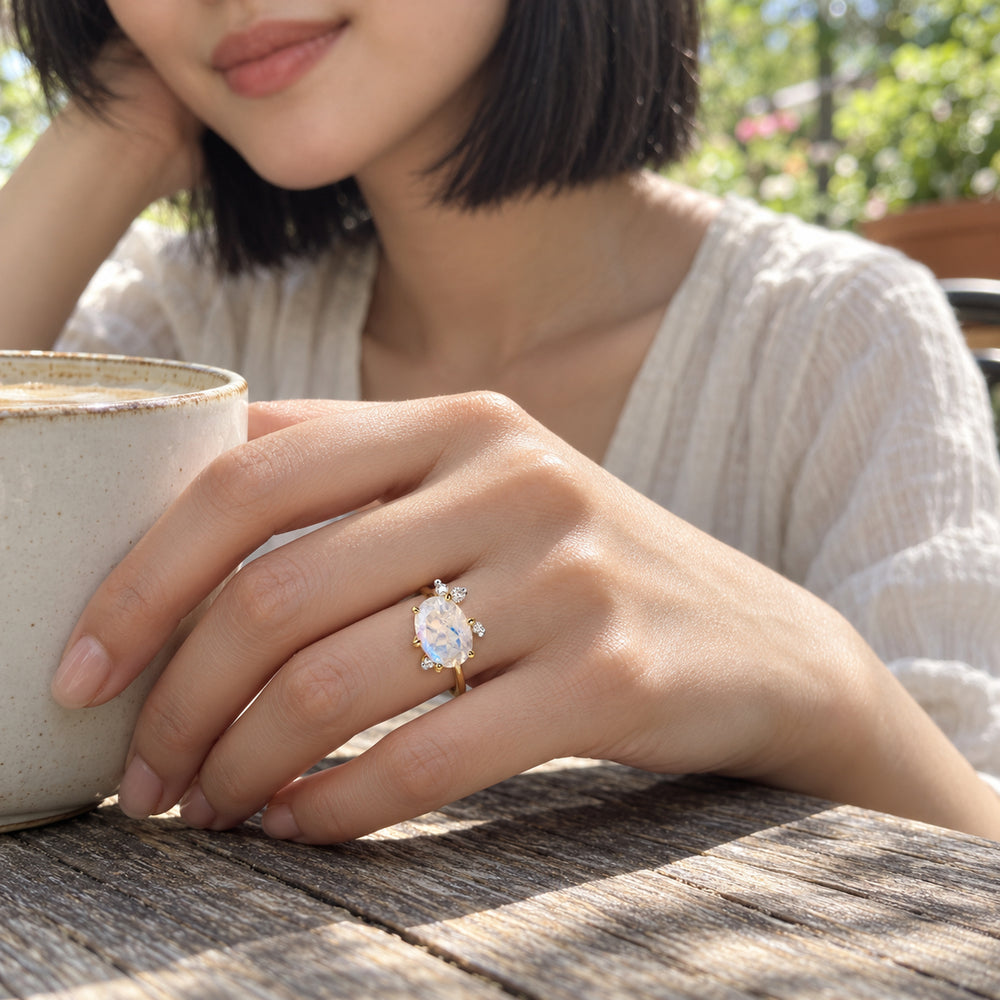 A woman wears the yellow gold moonstone ring while resting her hand beside a ceramic cup on a weathered wooden cafe table.