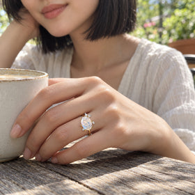 A woman wears the yellow gold moonstone ring while resting her hand beside a ceramic cup on a weathered wooden cafe table.