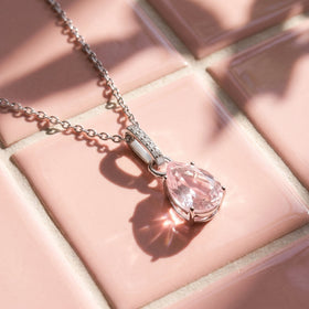Sunlight casts the shadow of a silver rose quartz pendant and its chain across a pink tiled surface.