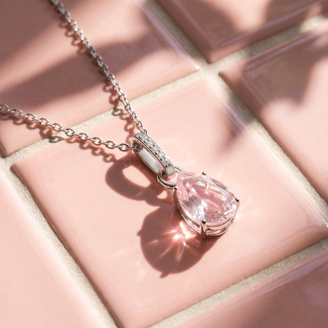 Sunlight casts the shadow of a silver rose quartz pendant and its chain across a pink tiled surface.