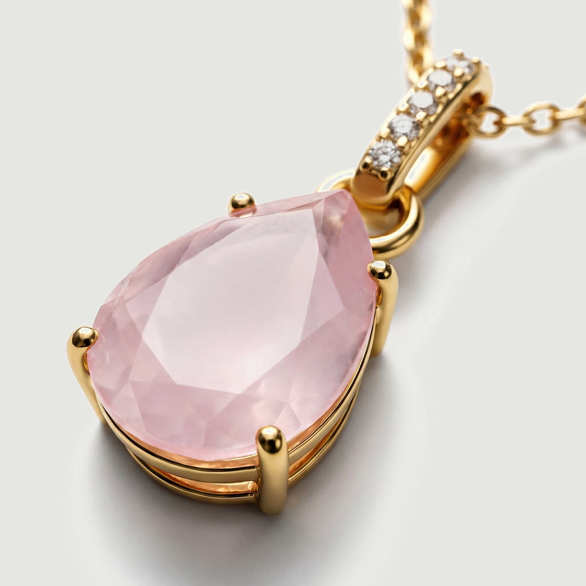 Four yellow gold prongs hold a pale pink pear-shaped stone below a bail set with clear round stones.